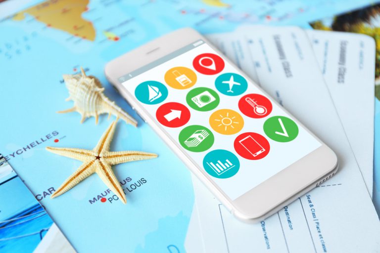 A phone with several travel apps on a map next to tropical items on a table