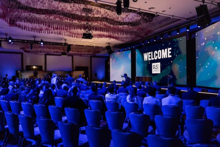 An audience seated in a large convention ballroom facing a stage with vibrant LED screens, illustrating the production and layout required when learning how to plan a corporate event.