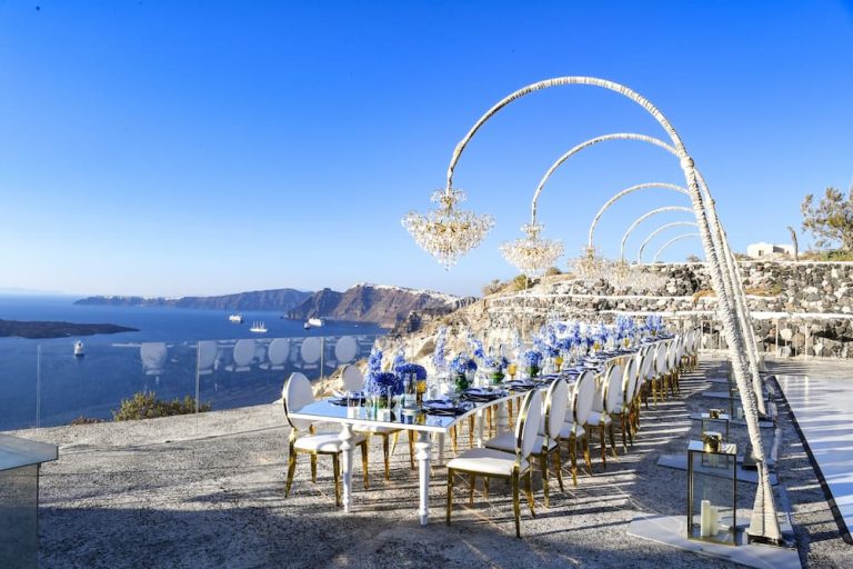 A luxury long dining table arranged on a cliffside terrace in Santorini overlooking the sea, showcasing a premium destination reward for a sales incentive travel program.